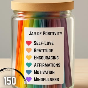 May include: A glass jar with a wooden lid filled with colorful paper strips. The jar has a label that reads "Jar of Positivity" and lists affirmations for self-love, gratitude, and more. The jar contains 150 affirmations.