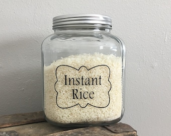 May include: A clear glass jar with a silver lid filled with white instant rice. The jar has a black label with the words "Instant Rice" in a decorative font.