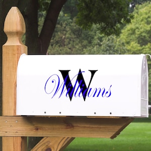 Op de afbeelding: Witte brievenbus met een zwarte en blauwe monogram sticker. De sticker heeft een grote zwarte letter "W" en het woord "Williams" in blauwe cursieve letters.
