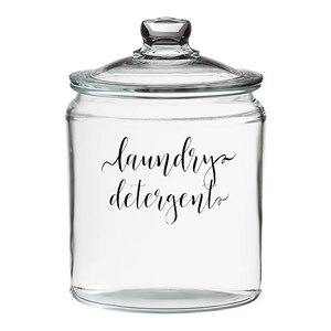 Op de afbeelding: Een glazen pot met deksel, met het opschrift "wasmiddel" in zwarte cursieve letters.