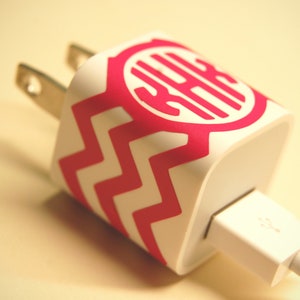 Op de afbeelding: Een witte telefoonlader met een roze en wit chevron-patroon en een roze monogram. De lader heeft een USB-connector.