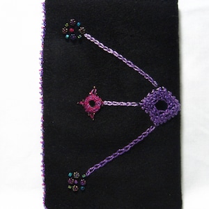 May include: Black felt crossbody bag with a beaded constellation design in purple and pink. The bag features a beaded border in shades of purple and pink, and a black strap. The design includes a square, a star, and a cluster of beads.
