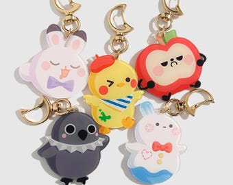 May include: A collection of six cartoon character keychains. The keychains feature a white bunny with a purple bow tie, a yellow chick with a red beret, a red apple, a gray bird, and a white bunny with a red bow tie and blue accents. Each keychain has a gold-colored clasp.