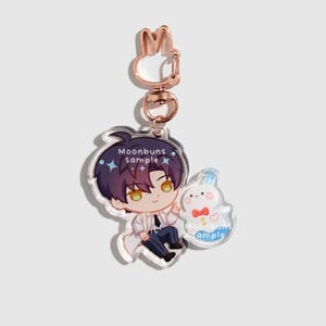 May include: An acrylic keychain featuring a chibi-style character with dark purple hair and yellow eyes, wearing a white coat and dark pants. Next to the character is a small white ghost-like figure with a red bow tie. It has a rose gold rabbit-shaped clasp.