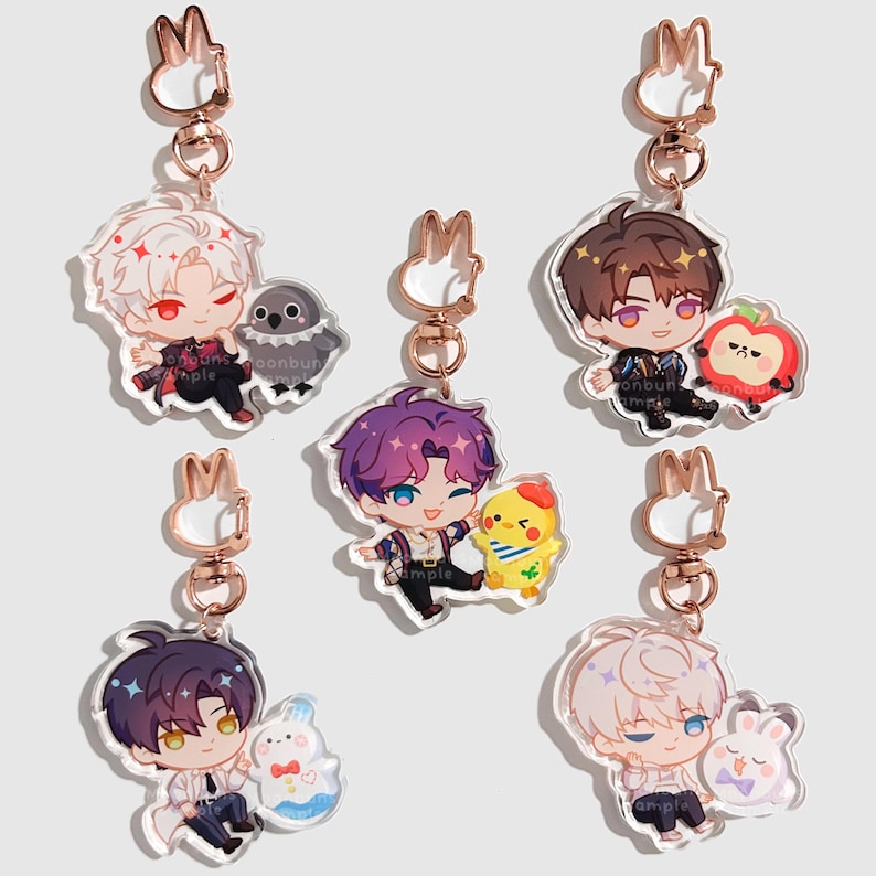 May include: Five acrylic keychains featuring chibi-style characters paired with small animal or fruit companions. Each charm has a rose gold-colored rabbit-shaped clasp. The characters have distinct hair colors and outfits, including white, brown, and purple.