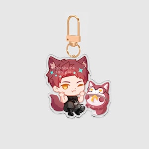 May include: An acrylic keychain featuring a cartoon character with red hair, wolf ears, and a tail, wearing a black tank top and pants. Beside the character is a small, round, red creature wearing glasses. The text moonbuns sample is visible.