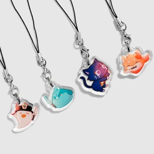 Puede incluir: Cuatro amuletos de personajes coloridos en correas de teléfono de cuerda negra. Los amuletos están hechos de acrílico transparente y presentan un gato azul y morado, un pájaro azul con un cuchillo, un fantasma con un cuchillo y un zorro naranja.
