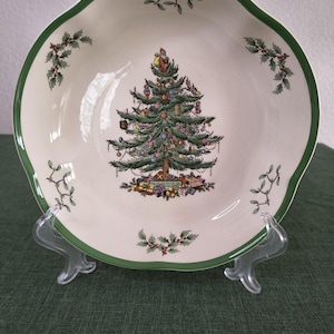 Puede incluir: Un cuenco de cerámica color crema con borde festoneado y ribete verde. El centro presenta un árbol de Navidad decorado con regalos debajo y Santa Claus en la cima. Ramas de acebo y muérdago están pintadas alrededor del borde interior.