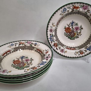 May include: A collection of vintage ceramic soup bowls. The bowls feature a white base, green rim, and a decorative border. Each bowl has a central floral design in various colours. A classic tableware set.