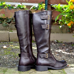 May include: A pair of brown leather knee-high boots with buckles and zippers. The boots have a chunky heel and a rounded toe.