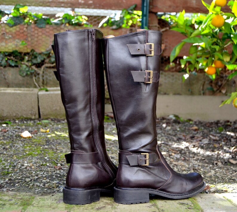 May include: A pair of brown leather knee-high boots with buckles and zippers. The boots have a chunky heel and a rounded toe.