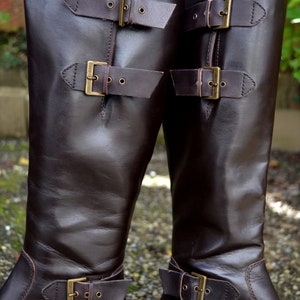 May include: A pair of brown leather knee-high boots with multiple buckles. The boots have a smooth leather finish and a pointed toe.
