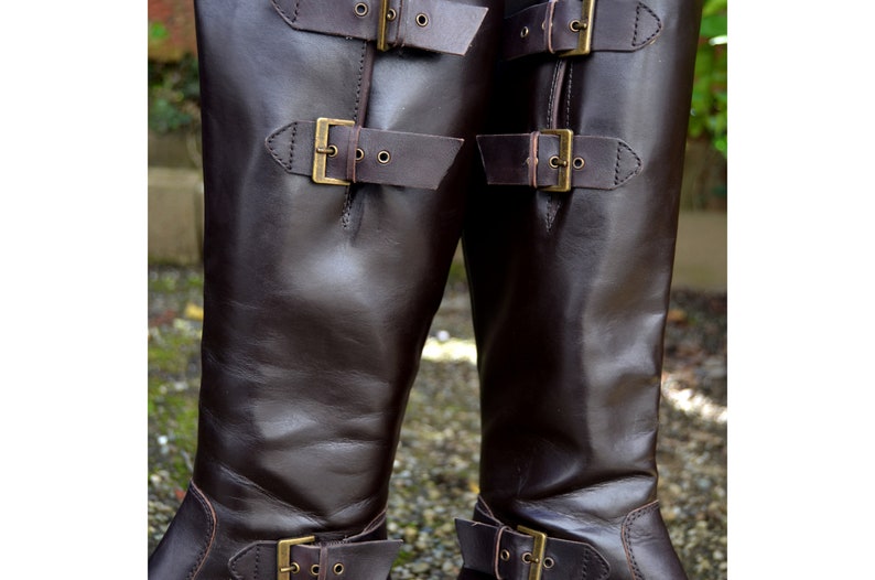 May include: A pair of brown leather knee-high boots with multiple buckles. The boots have a smooth leather finish and a pointed toe.