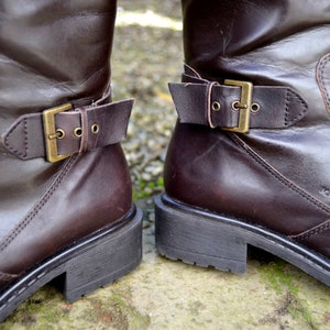 May include: A pair of brown leather boots with buckles. The boots have a stitched seam on the side and the brand name "Kare" is visible on the right boot.