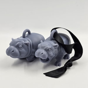 May include: Two grey hippopotamus figurines, one with a black ribbon attached. The hippopotamus figurines are detailed and have a realistic appearance.