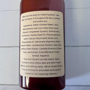 Puede incluir: Una botella marr&oacute;n con una etiqueta que detalla los ingredientes e instrucciones de uso de una bruma corporal. La etiqueta enumera ingredientes como jugo de aloe vera, glicerina y hamamelis. El texto describe las propiedades hidratantes y calmantes de la bruma.