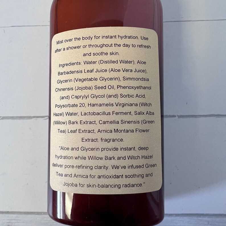 Puede incluir: Una botella marr&oacute;n con una etiqueta que detalla los ingredientes e instrucciones de uso de una bruma corporal. La etiqueta enumera ingredientes como jugo de aloe vera, glicerina y hamamelis. El texto describe las propiedades hidratantes y calmantes de la bruma.