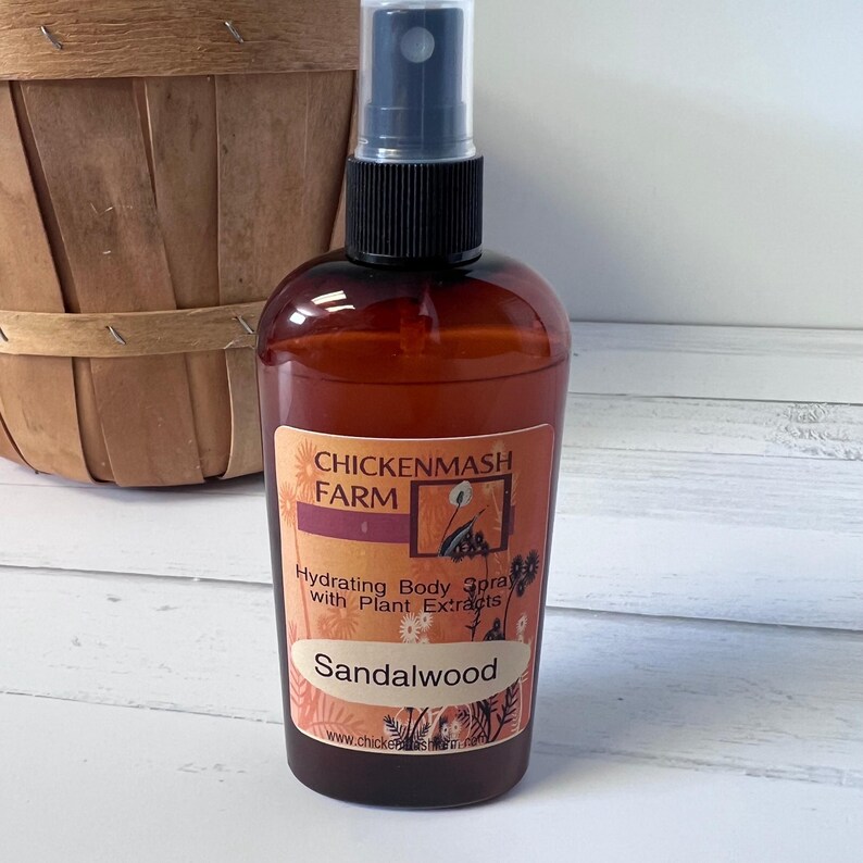 Puede incluir: Una botella de vidrio marr&oacute;n de spray hidratante para el cuerpo con un pulverizador negro. La etiqueta dice "Chickenmash Farm" y "Sandalwood". La botella est&aacute; frente a una cesta de madera.