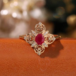 May include: A gold ring with a red ruby gemstone surrounded by smaller diamonds in a delicate, ornate design.