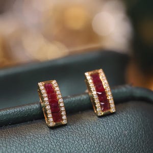 May include: A pair of gold earrings with a row of red gemstones and a border of smaller white gemstones.