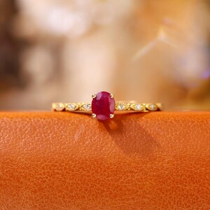 May include: A gold ring with a red oval gemstone surrounded by smaller white gemstones.