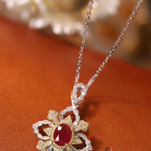 Puede incluir: Un delicado collar de oro y plata con un colgante floral engastado con un rubí rojo. El colgante está rodeado de diamantes más pequeños.