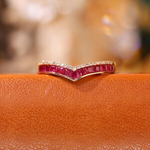 以下が含まれることがあります： V字型の赤いルビーの列と小さな透明な石が並んだゴールドのバンドリングです。
