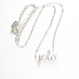 May include: A silver chain necklace with a silver wire pendant that says "yolo".