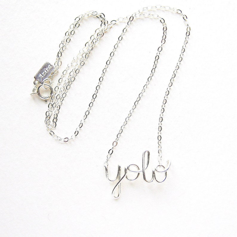 May include: A silver chain necklace with a silver wire pendant that says "yolo".