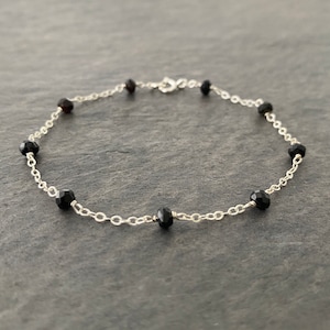 May include: A delicate silver chain bracelet with black gemstone beads. The bracelet is approximately 7 inches in length and features a lobster clasp closure.
