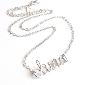 May include: A silver chain necklace with the name "Laura" spelled out in cursive script.