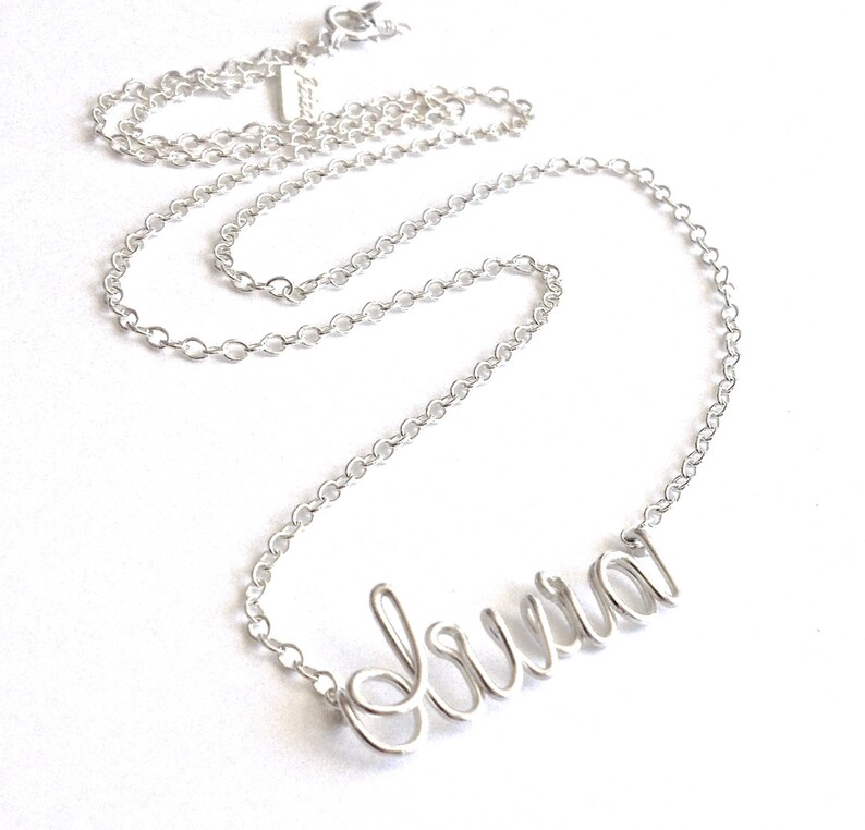 May include: A silver chain necklace with the name "Laura" spelled out in cursive script.