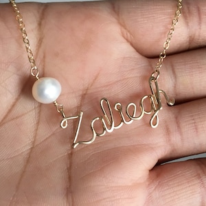 May include: Gold necklace with a pearl charm and the name "Zaliegh" written in cursive.