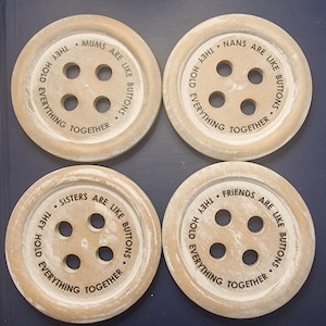 May include: Four round wooden coasters with a button design. Each coaster has a different saying about family members. The sayings are "Mums are like buttons, they hold everything together", "Nans are like buttons, they hold everything together", "Sisters are like buttons, they hold everything together", and "Friends are like buttons, they hold everything together".