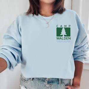 A woman wearing a light blue sweatshirt with a logo for Camp Walden printed on it.