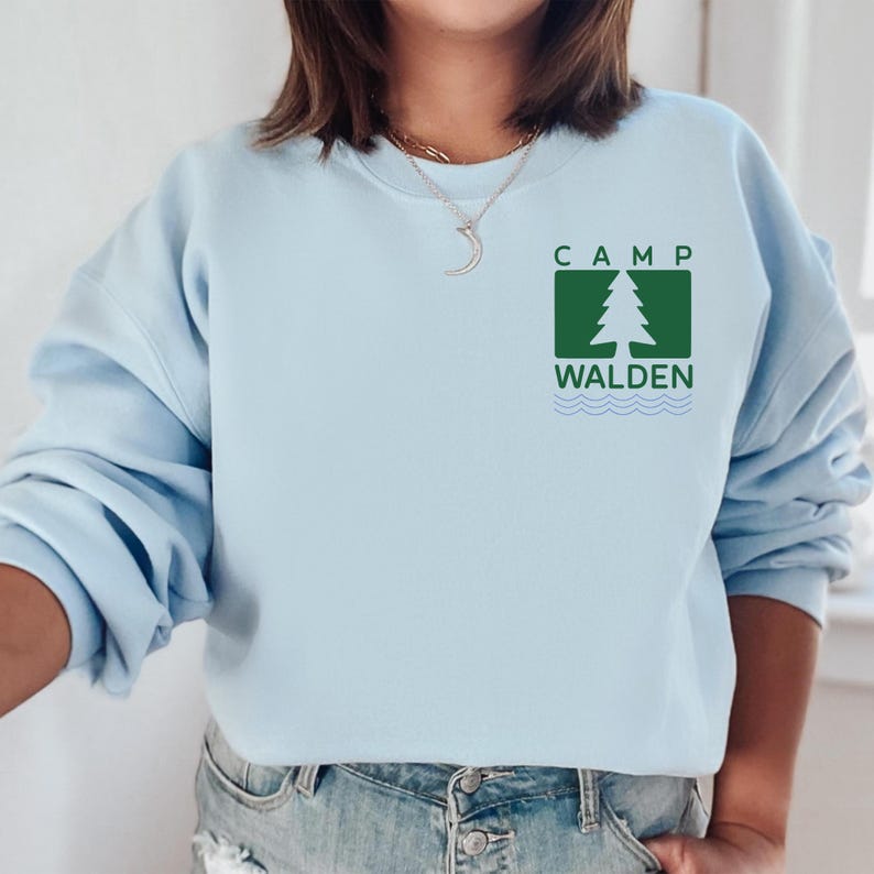 A woman wearing a light blue sweatshirt with a logo for Camp Walden printed on it.