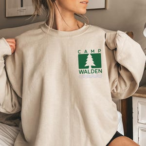 A woman wearing a beige sweater with a green logo on the front.