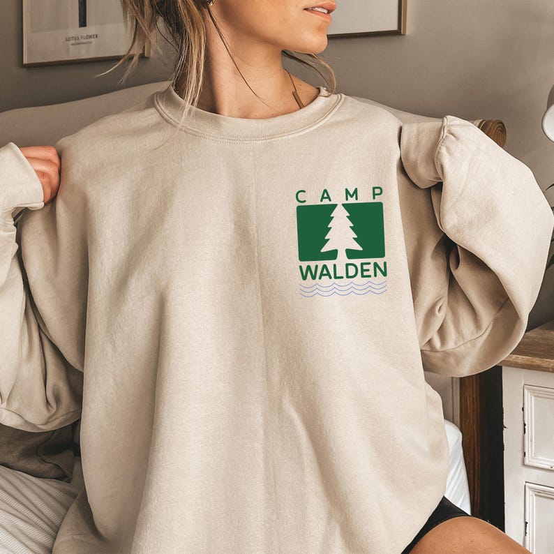A woman wearing a beige sweater with a green logo on the front.