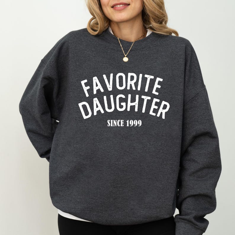 A woman wearing a gray sweatshirt with the text "Favored Daughter Since 1999" printed on it.