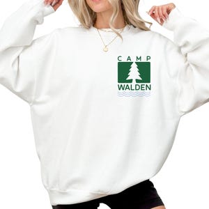 A woman wearing a white sweatshirt with a green and white logo on the front.