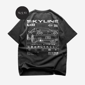 Könnte beinhalten: Ein schwarzes Kurzarm-T-Shirt mit einem weißen Grafikdruck auf der Rückseite. Das Design zeigt eine Illustration eines Nissan Skyline R34, den Text "SKYLINE", "LEGENDS NEVER DIE", "伝説は決して死なない", "nismo" sowie technische Fahrzeugdaten.