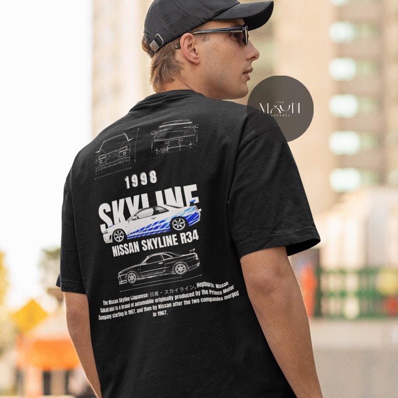 May include: Black t-shirt with a white graphic of a Nissan Skyline R34 car. The graphic includes the text "1998 SKYLINE" and "NISSAN SKYLINE R34". The t-shirt also features a small white graphic of the car's side profile.