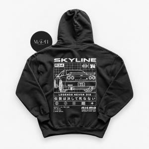 May include: A black hooded sweatshirt featuring a white graphic on the back. The design displays a Nissan Skyline R34 car illustration, the text SKYLINE, R34, GT-R, LEGENDS NEVER DIE, 伝説は決して死なない, and nismo. Technical specifications are listed below the car.