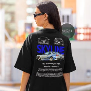 May include: Black t-shirt with a blue and white graphic of a Nissan Skyline R34 car. The text "SKYLINE" is printed in blue above the car. The text "The Nissan Skyline R34 - Nissan has a rich history." is printed below the car.