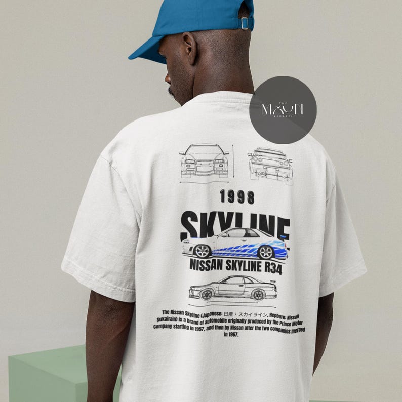 May include: White t-shirt with a black and white illustration of a Nissan Skyline R34 car. The text "1998 SKYLINE" is printed in black above the car. The text "NISSAN SKYLINE R34" is printed in black below the car. The text "The Nissan Skyline (Japanese: 日産・スカイライン, Hepburn: Nissan Sukairain) is a brand of automobile originally produced by the Prince Motor Company starting in 1957, and then by Nissan after the two companies merged in 1967." is printed in black below the car.