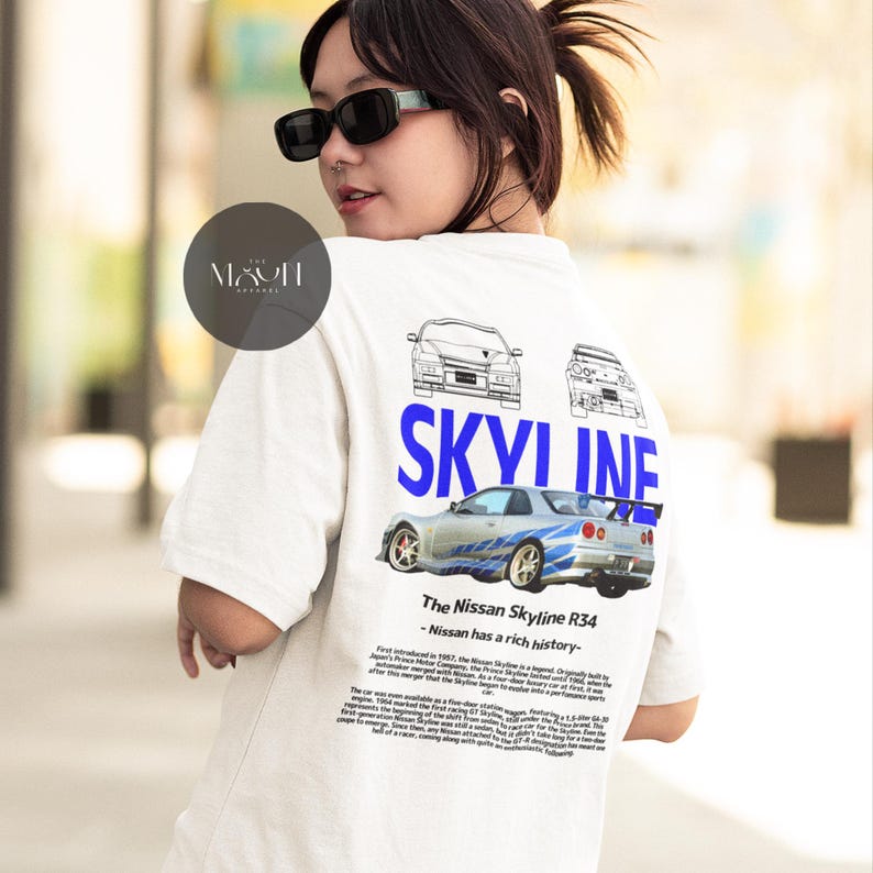 May include: White t-shirt with a blue and white graphic of a Nissan Skyline R34 car. The text "SKYLINE" is printed in blue above the car. The text "The Nissan Skyline R34 - Nissan has a rich history" is printed below the car.