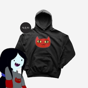 Pode incluir: Moletom preto com capuz com um gráfico de rosto de gato vermelho. O gato tem olhos amarelos e sardas. O gráfico está na frente do moletom. Possui um bolso canguru e um capuz com cordão.