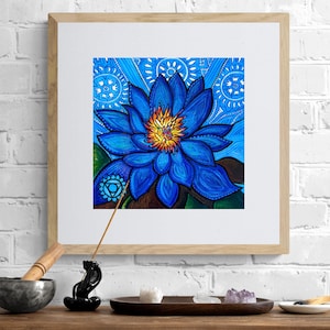 Può includere: Una stampa artistica incorniciata con un vibrante fiore di loto blu con un centro giallo. L'opera d'arte è ambientata su uno sfondo blu a motivi. La stampa è esposta in una cornice di legno chiaro.
