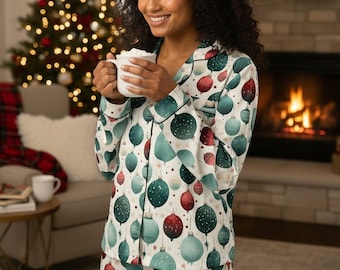 May include: A long-sleeved button-down pajama top in white featuring a repeating pattern of Christmas ornaments in shades of red, dark green, and light teal. The garment includes a notched collar and dark green piping along the edges.
