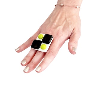 Könnte beinhalten: Ein weißer, schwarzer und grüner Glasring mit geometrischem Design. Der Ring wird an einem Finger getragen.